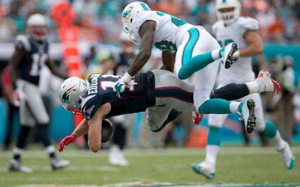 Action-packed HD desktop wallpaper featuring a Miami Dolphins player tackling a New England Patriots player during a football game, showcasing dynamic sports intensity.
