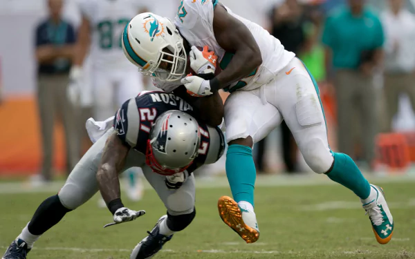 Action-packed HD desktop wallpaper featuring Miami Dolphins player tackling a New England Patriots defender during an intense NFL game.