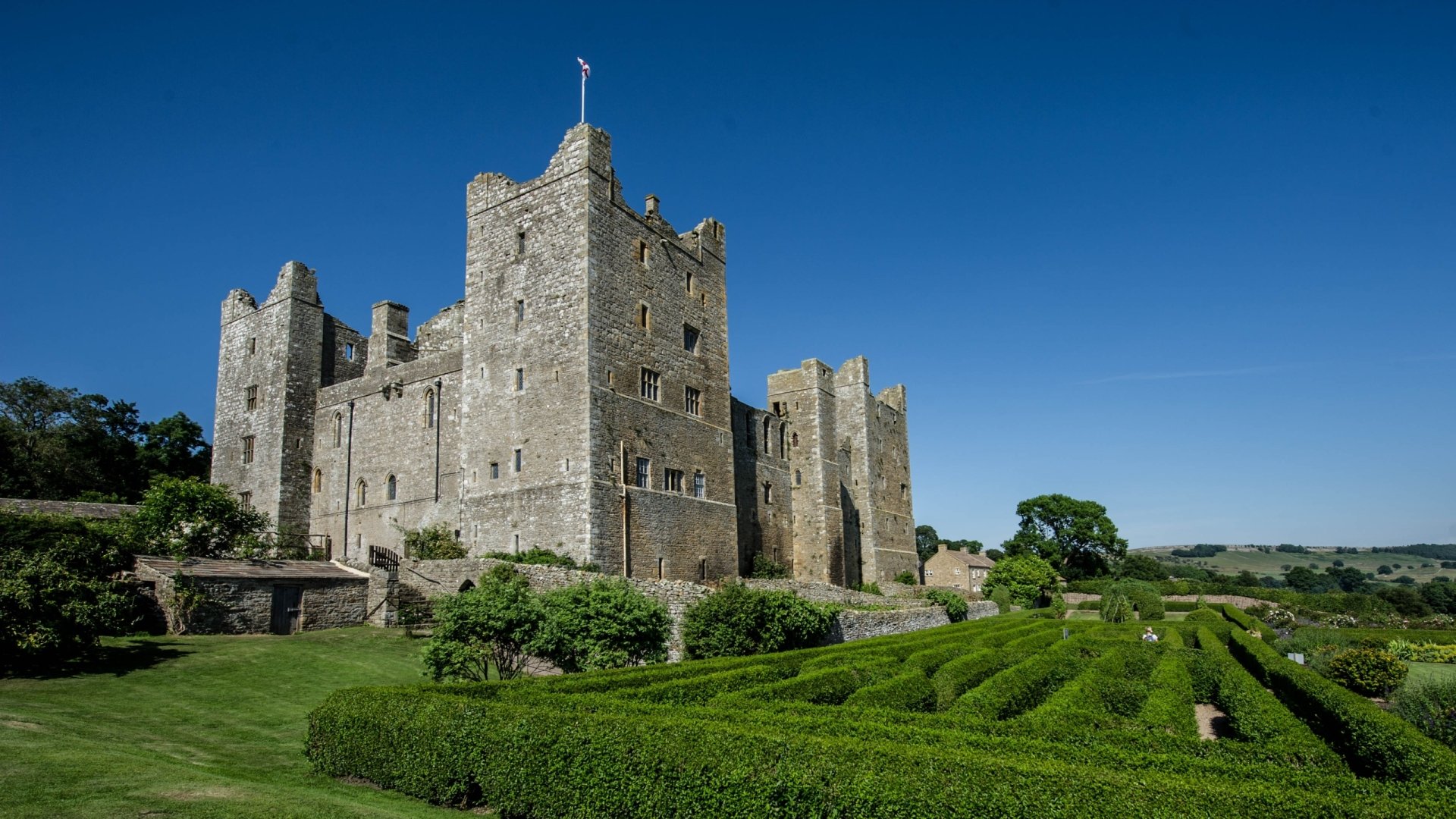 HD desktop wallpaper featuring the man-made Bolton Castle surrounded by lush greenery under a clear blue sky.