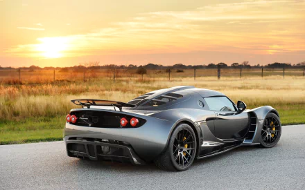 A striking silver Hennessey Venom GT supercar parked on a scenic road at sunset, showcasing its sleek design against a backdrop of golden fields.