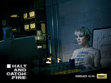 Halt and Catch Fire HD PC desktop wallpaper: moody tech workspace with a short-haired person seated at a cluttered desk, CRT monitor glow, shelving and a whiteboard in a dimly lit room.