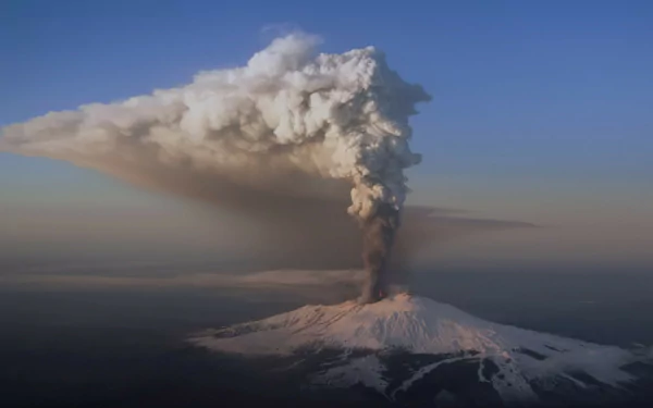 HD desktop wallpaper showing a volcanic eruption with thick smoke billowing into the clear sky, capturing the raw power of nature.