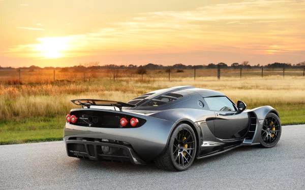 A striking silver Hennessey Venom GT supercar parked on a scenic road at sunset, showcasing its sleek design against a backdrop of golden fields.