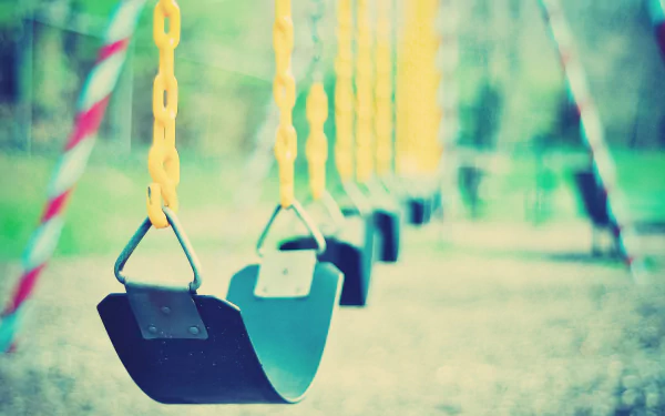 A vibrant HD desktop wallpaper featuring a row of swings with yellow chains, set against a softly blurred, natural background, evoking a sense of nostalgia and playfulness.