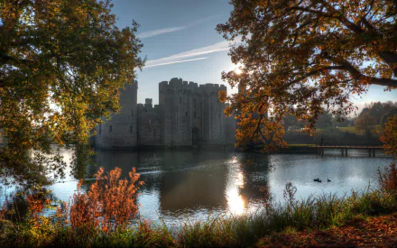 Man-made Bodiam Castle reflected in a calm moat, framed by autumn trees and reeds — 2K Quad HD PC desktop wallpaper background.