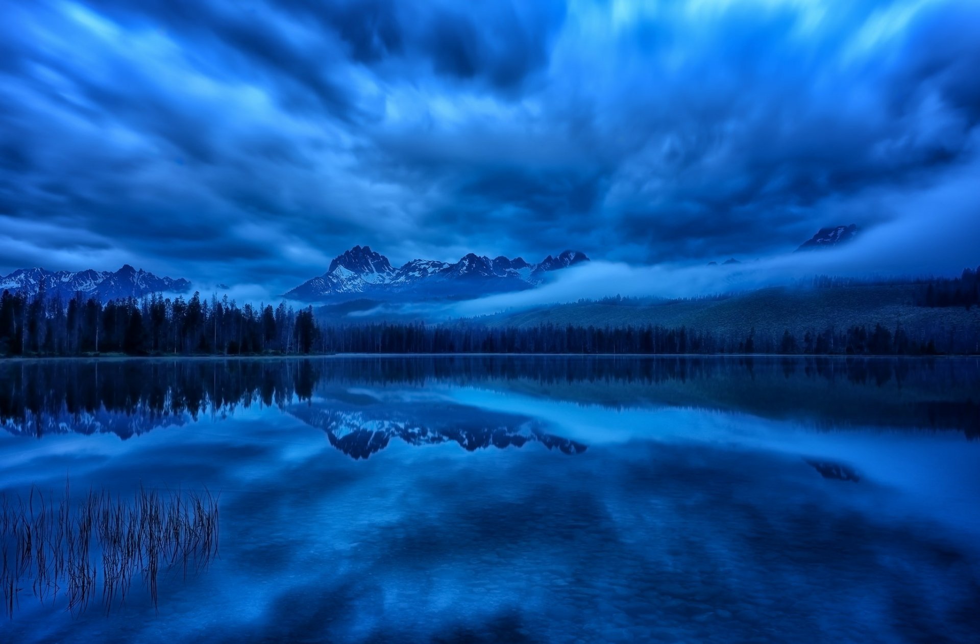 Twilight view of the Sawtooth Mountains and clouds reflected in a calm lake at Sawtooth National Recreation Area, Idaho, captured in a vivid HD desktop wallpaper.