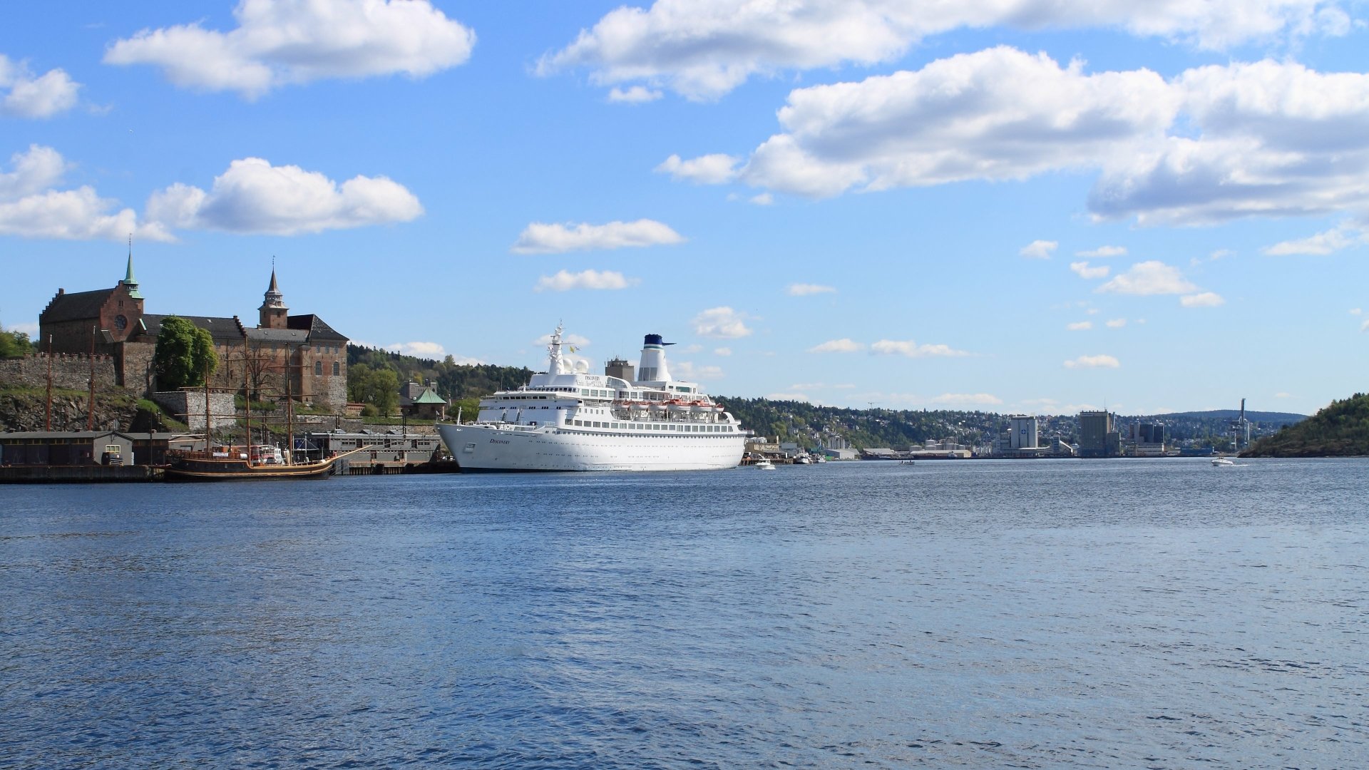 4K Ultra HD PC desktop wallpaper of a cruise ship vehicle docked by a coastal town, calm blue sea and sky with scattered clouds.