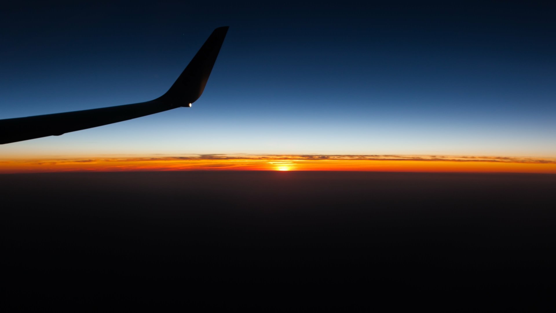 4K Ultra HD PC desktop wallpaper: silhouetted airplane wing above a glowing orange sunset on the horizon.