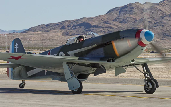 HD desktop wallpaper of a Yakovlev Yak-3 military aircraft on a runway with mountainous terrain in the background.