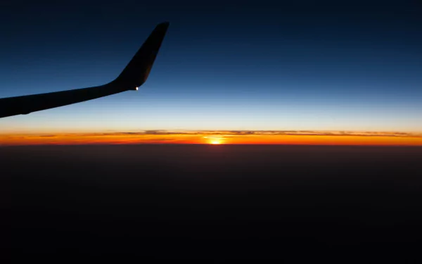 4K Ultra HD PC desktop wallpaper: silhouetted airplane wing above a glowing orange sunset on the horizon.