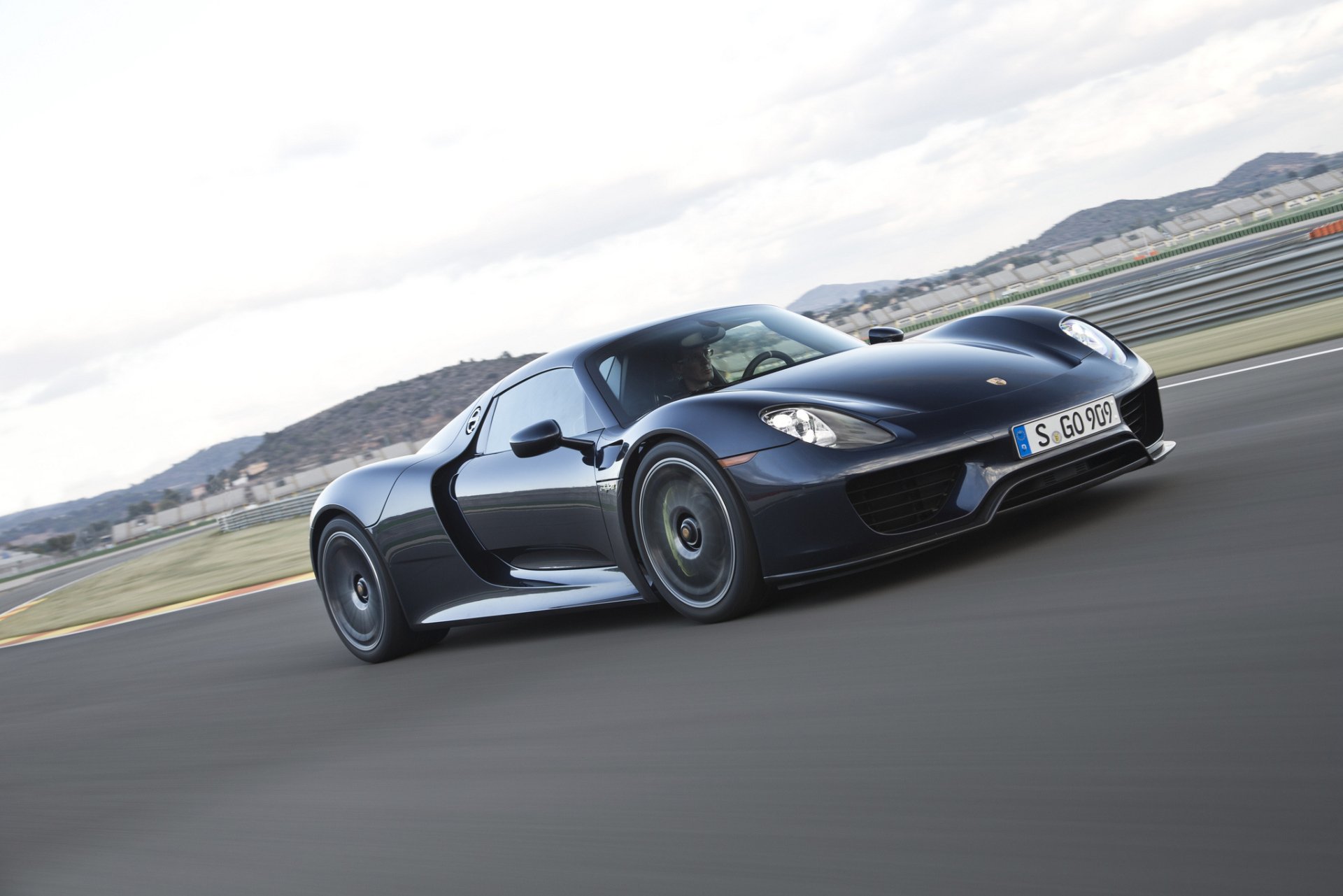 Black Porsche 918 Spyder vehicle accelerating on a racetrack with rolling hills — HD PC desktop wallpaper background.