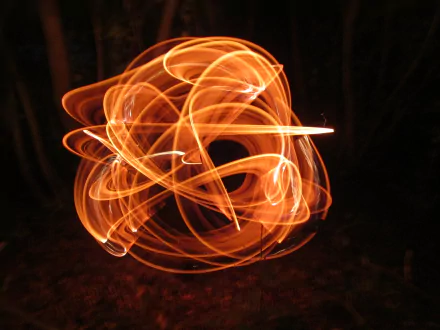 A vibrant 4K Ultra HD photography wallpaper capturing the dynamic motion of fire juggling, with swirling trails of bright orange flames against a dark background.
