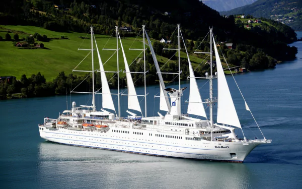 HD desktop wallpaper of a white sailboat with multiple sails sailing on calm water, surrounded by green hills and mountains in the background.