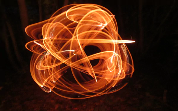 A vibrant 4K Ultra HD photography wallpaper capturing the dynamic motion of fire juggling, with swirling trails of bright orange flames against a dark background.