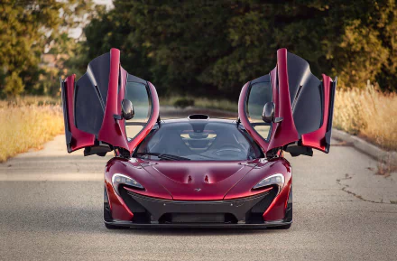 A striking crimson McLaren P1 with its iconic gullwing doors raised, set against a natural backdrop, creating an impressive HD desktop wallpaper.