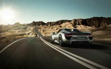 Rear view of a silver Porsche 918 Spyder speeding along a winding desert road under a bright sun — HD PC desktop wallpaper and background.