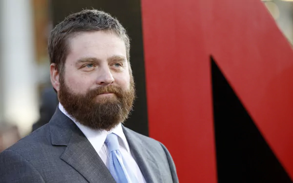 HD wallpaper featuring a bearded man in a suit at an event, standing before a red backdrop.