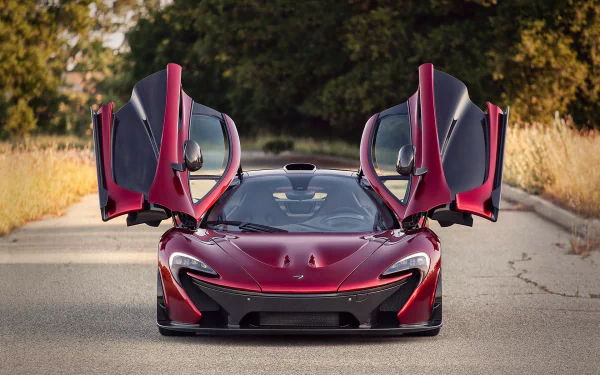A striking crimson McLaren P1 with its iconic gullwing doors raised, set against a natural backdrop, creating an impressive HD desktop wallpaper.