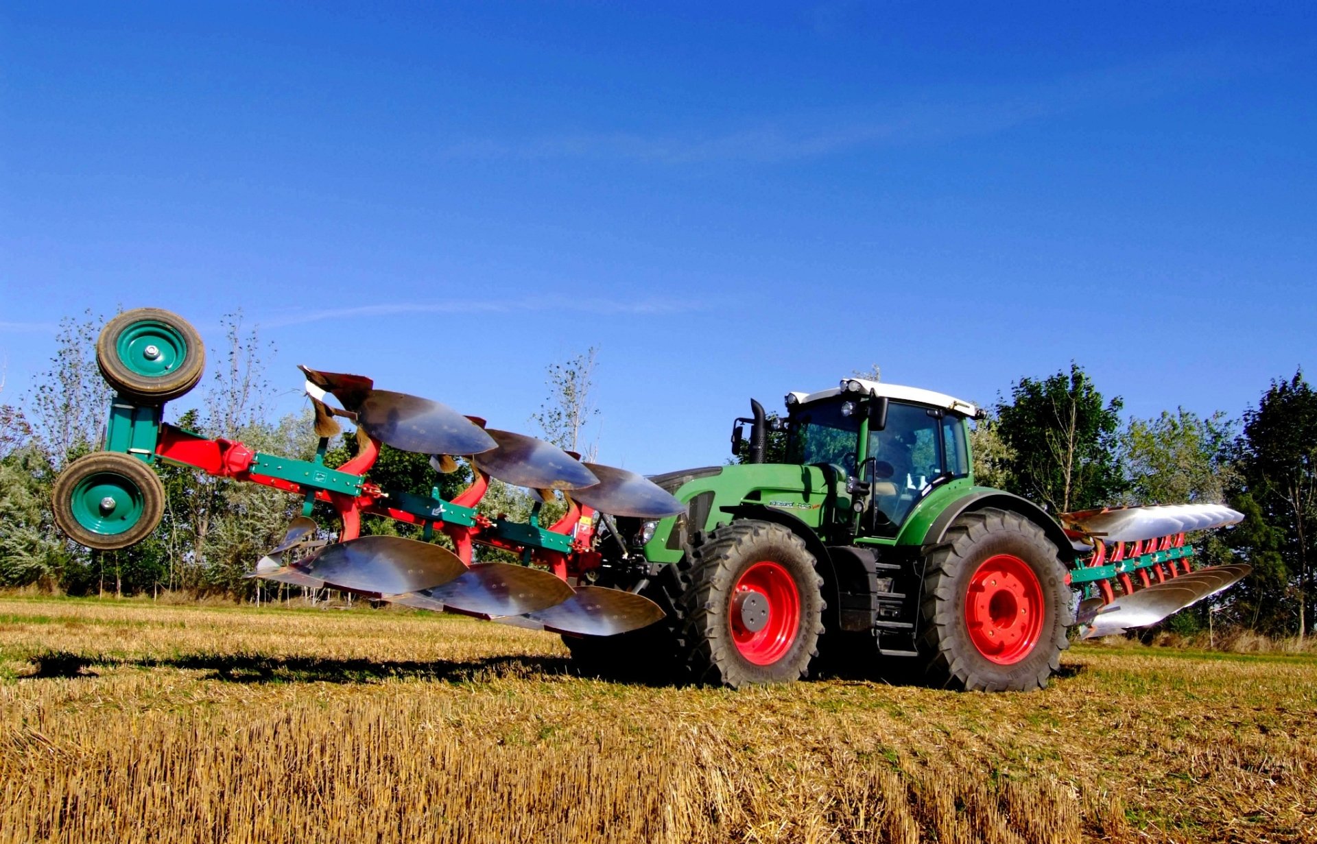 HD PC desktop wallpaper and background: green Claas tractor vehicle pulling a wide multi-furrow plow across a harvested golden field under a clear blue sky.