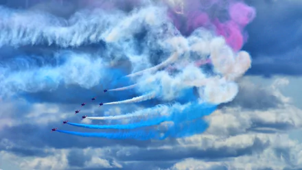 HD PC desktop wallpaper showing a military air show with jets creating colorful smoke trails against a cloudy sky.