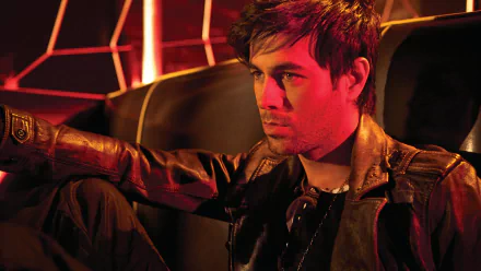 Enrique Iglesias poses confidently in a leather jacket against a vibrant red backdrop, creating a striking HD desktop wallpaper for music fans.