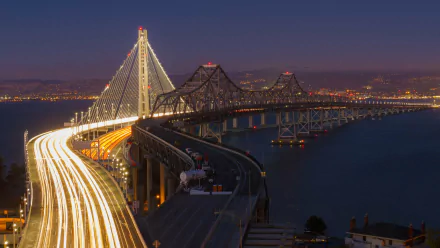 Nighttime view of the Bay Bridge connecting Oakland and San Francisco, captured in stunning 4K Ultra HD with city lights glowing in the background.