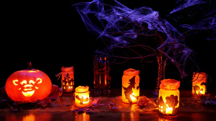A vibrant HD wallpaper showcasing Halloween decorations, featuring lit candles in jars and a carved pumpkin, with festive holiday ornaments and spooky webs creating a festive atmosphere.