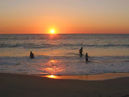 Sunrise over the ocean with people swimming near the sandy beach, captured in a vibrant HD desktop wallpaper showcasing sun, water, and serene morning light.