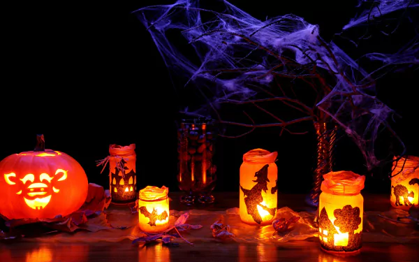 A vibrant HD wallpaper showcasing Halloween decorations, featuring lit candles in jars and a carved pumpkin, with festive holiday ornaments and spooky webs creating a festive atmosphere.