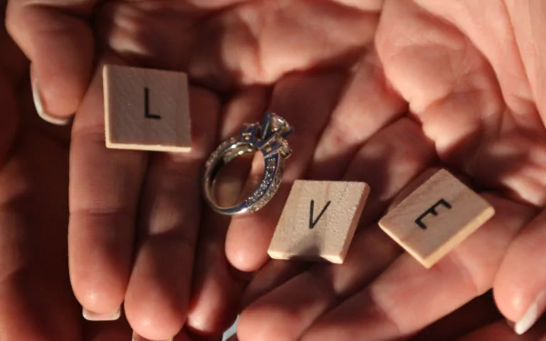 HD desktop wallpaper of hands holding wooden letter tiles forming the word LOVE with an engagement ring, conveying an artistic expression of love.