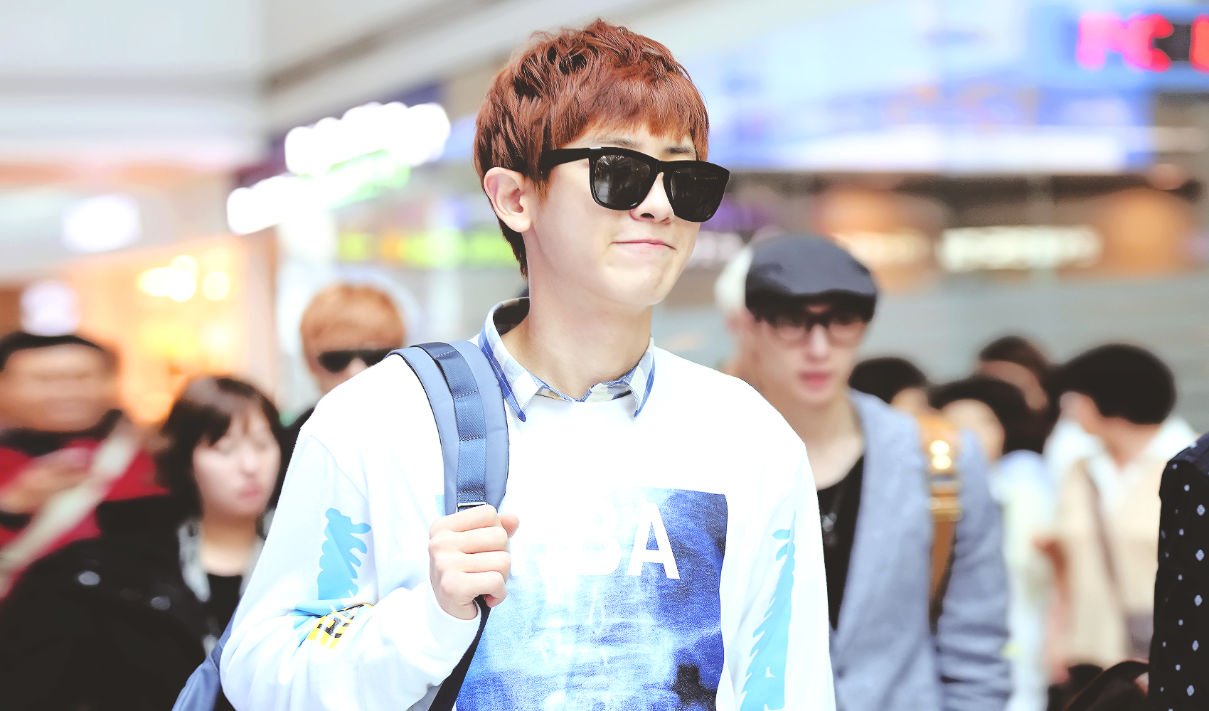 A stylish individual wearing sunglasses and a graphic sweater walks through a bustling crowd, capturing a vibrant moment. This HD wallpaper features a theme related to EXO.