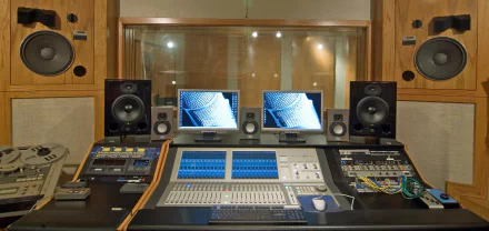 A modern music studio featuring a professional mixing console, dual monitors, and studio monitors, designed for creating and recording high-quality sound.