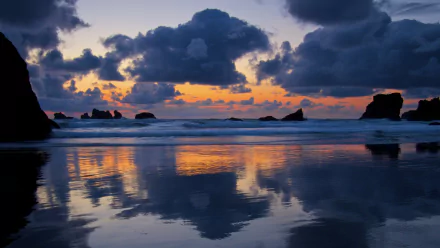 4K Ultra HD seascape wallpaper showcasing a vibrant sunset with dark clouds reflecting over calm ocean waters and silhouetted rocky formations along the shore.