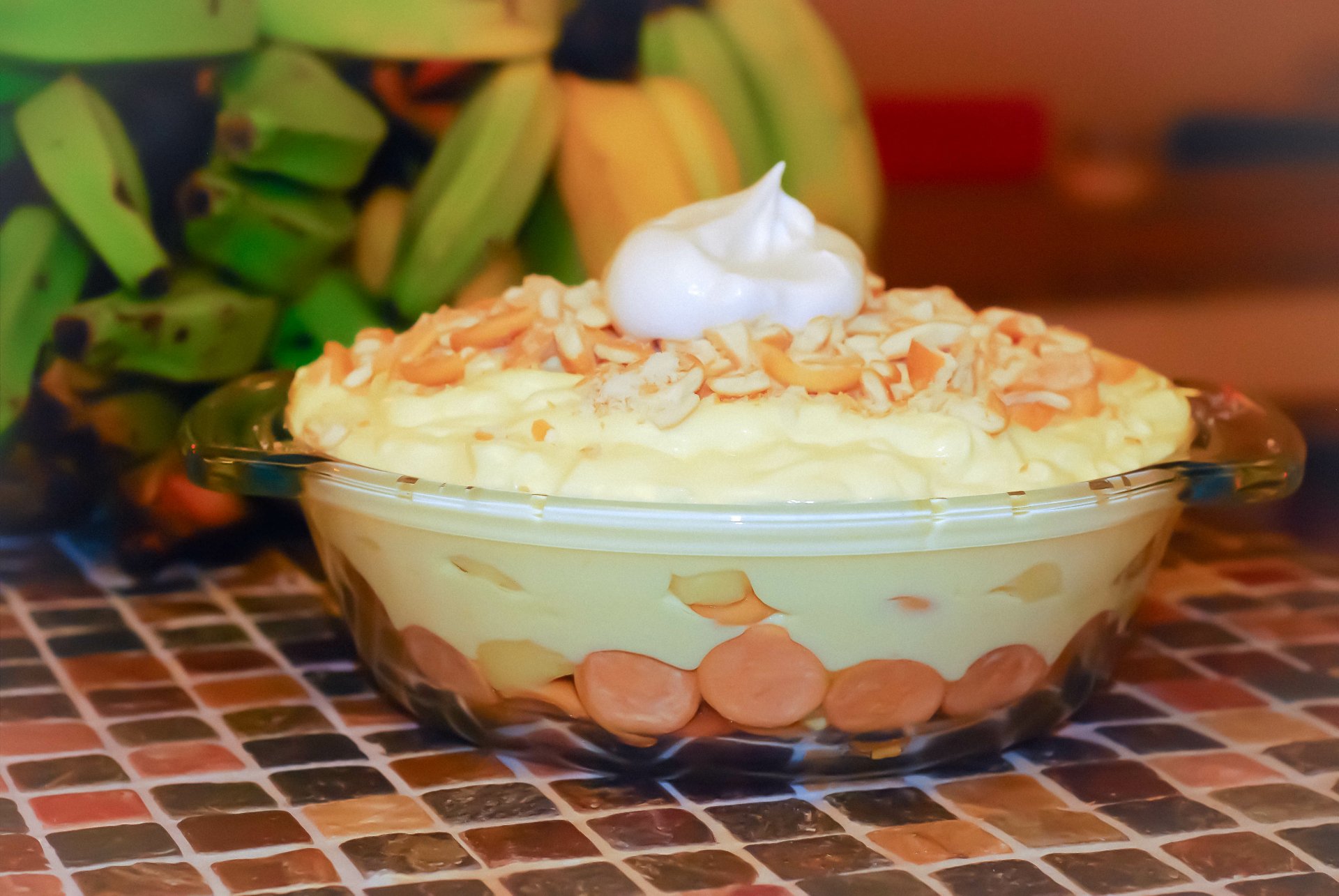 A close-up 4K Ultra HD wallpaper of creamy banana pudding topped with toasted coconut and whipped cream, with fresh bananas blurred in the background.