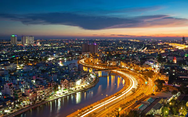 A vibrant aerial view of Ho Chi Minh City at dusk, showcasing the Saigon River winding through the illuminated urban landscape in Vietnam.