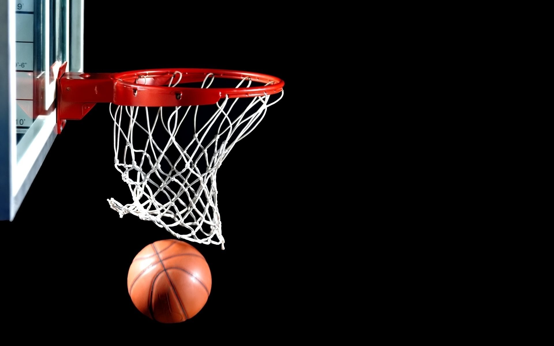 A basketball is about to pass through a red hoop, set against a black background, capturing the energy of the game. This HD image serves as a vibrant desktop wallpaper for sports enthusiasts.