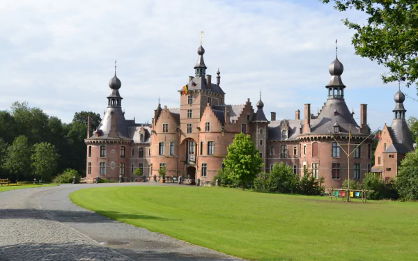 HD desktop wallpaper of the man-made Ooidonk Castle, showcasing its detailed architecture surrounded by green lawns and trees under a clear sky.