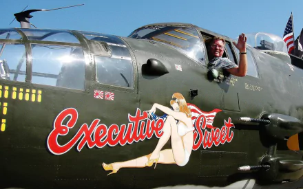 HD military aircraft nose art featuring a vintage bomber with a pin-up girl illustration and the text Executive Sweet, set against a clear blue sky background.