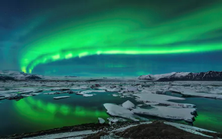 HD wallpaper of the northern lights (aurora borealis) illuminating a snowy landscape at night, reflecting over icy waters.