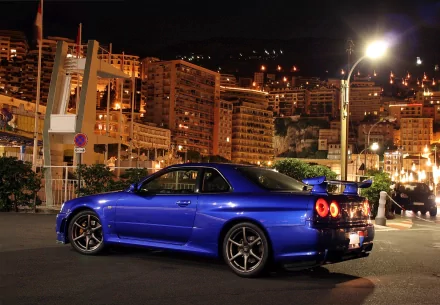 A striking blue Nissan Skyline GT-R parked at night, illuminated by city lights, showcasing its sleek design in a vibrant urban setting.