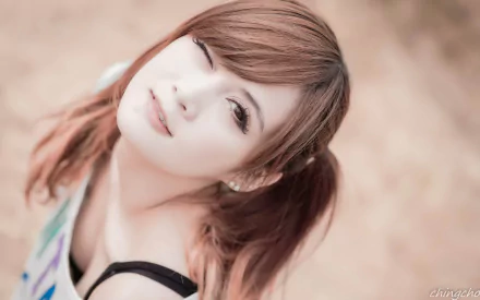 HD desktop wallpaper featuring an Asian woman with auburn hair in pigtails, winking at the camera in a soft, neutral background.