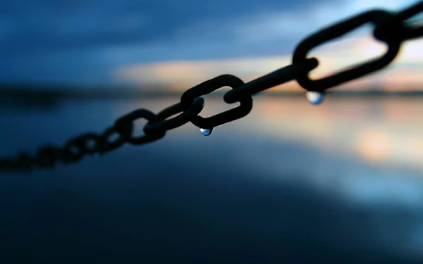 A close-up of a metal chain with a droplet of water clinging to it, set against a serene, blurred background of water and sky, providing an aesthetic touch for a desktop wallpaper.