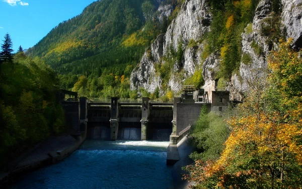 A stunning HD wallpaper featuring a man-made dam nestled between towering mountains and vibrant autumn foliage, with a serene river flowing beneath.