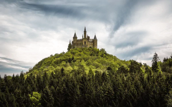 Hohenzollern Castle perched atop a lush green hill under a dramatic cloudy sky, captured in a high-definition desktop wallpaper.
