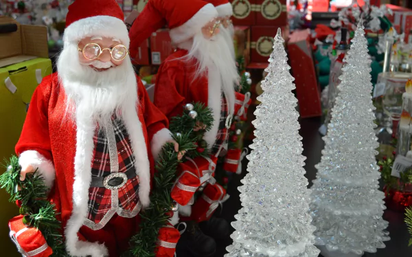 Two cheerful Santas in red outfits stand beside sparkling holiday trees, surrounded by colorful Christmas ornaments, creating a festive store atmosphere perfect for the season.