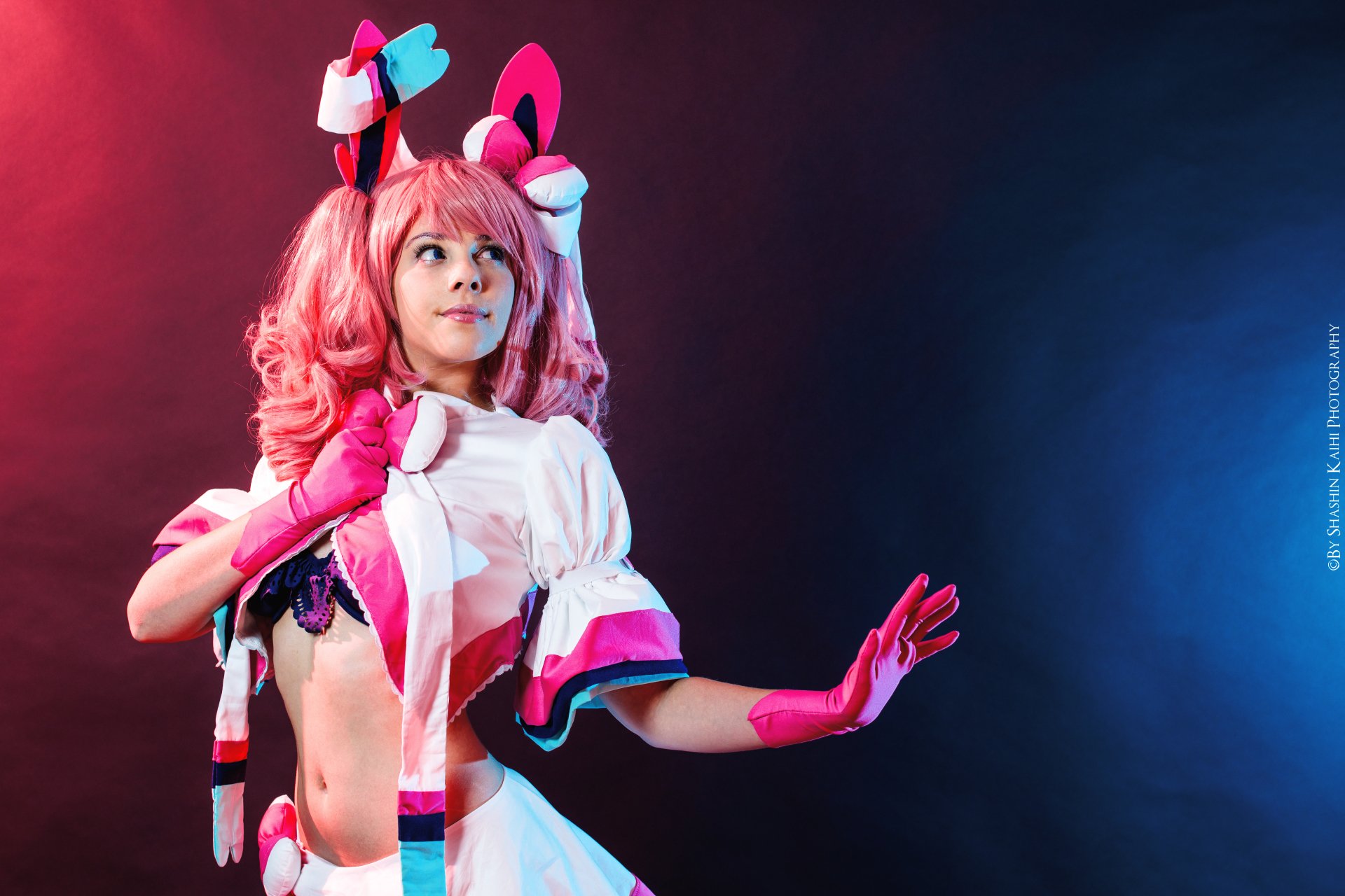 A woman in vibrant cosplay poses confidently against a dark background, featuring colorful lighting. An engaging HD desktop wallpaper showcasing creativity and character.