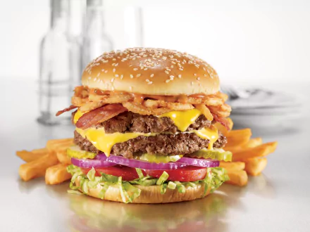 A juicy burger with melted cheese, crispy bacon, fresh vegetables, and onion rings, served with golden fries. This vibrant image is a stunning 4K Ultra HD desktop wallpaper.