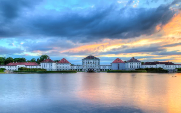 HD PC desktop wallpaper: Nymphenburg Palace, a man-made Baroque palace mirrored in calm water at sunset beneath dramatic clouds.