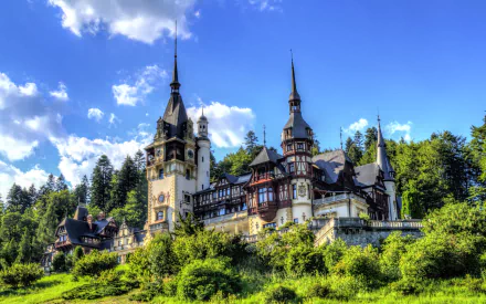 Peles Castle in Romania stands majestically in summer, surrounded by lush greenery, showcasing stunning architecture against a bright blue sky. An impressive man-made landmark.