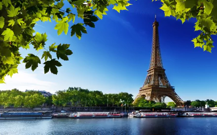 HD desktop wallpaper of the Eiffel Tower in Paris, France, under a clear blue sky, with lush green trees and a serene river in the foreground.